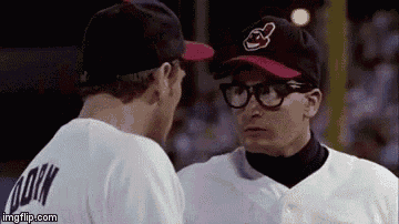two baseball players , one wearing glasses and a hat , are looking at each other .