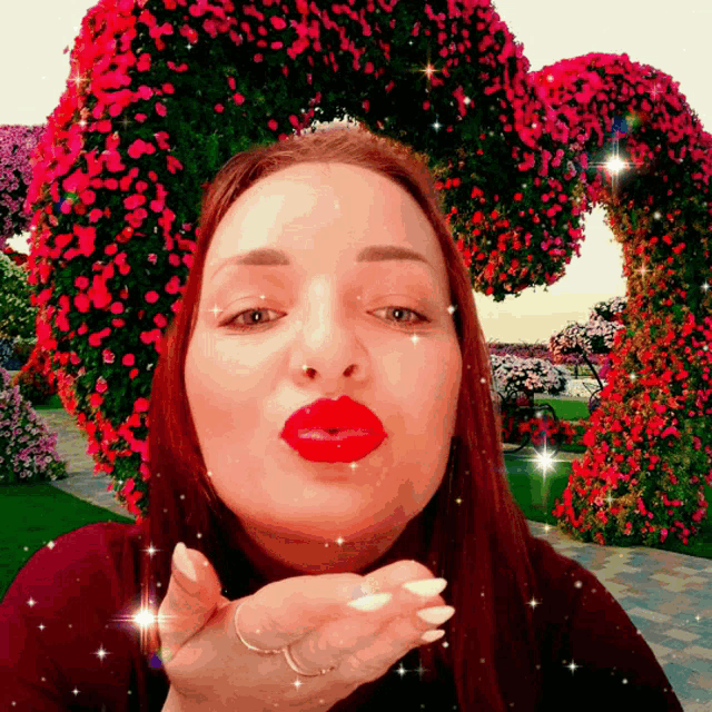 a woman with red lips blowing a kiss in front of a heart shaped flower display