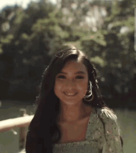 a woman is smiling and looking at the camera while standing in front of a lake .