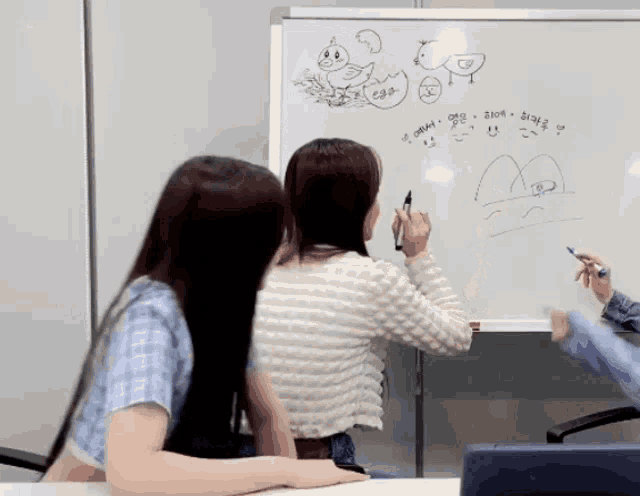two women are drawing on a whiteboard with a duck and a duck egg