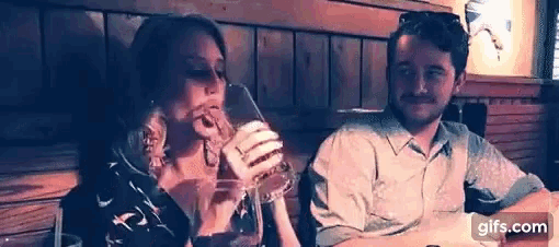 a man and a woman are sitting at a table drinking from a glass .