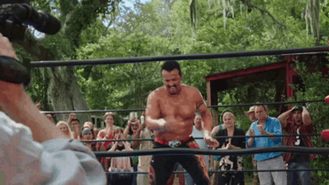 a man without a shirt is in a wrestling ring with a crowd watching