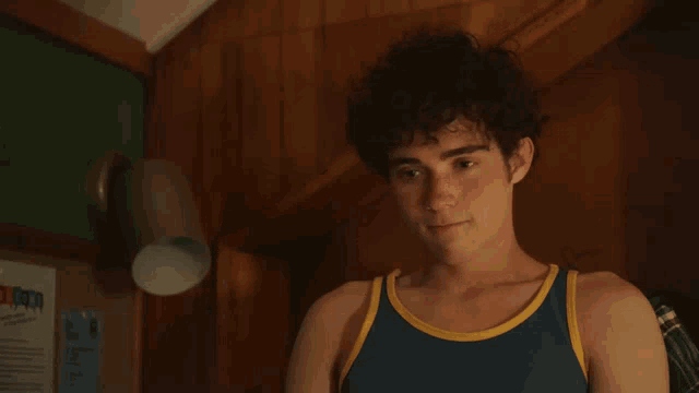 a young man in a blue tank top is standing in front of a bulletin board that says ' autumn '