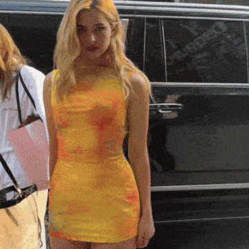 a woman in a yellow tie dye dress stands in front of a black van that says dsquared on the side