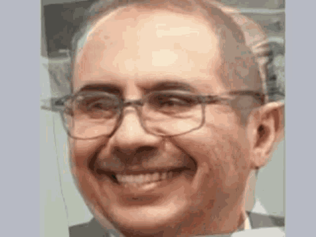 a man wearing glasses and a suit is smiling for the camera .