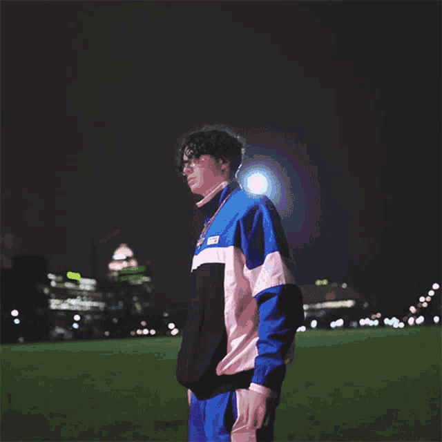 a man wearing a jacket that says ' nb ' on it is standing on a field at night