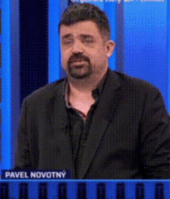a man with a beard is standing in front of a blue board with the name pavel novotny written on it .