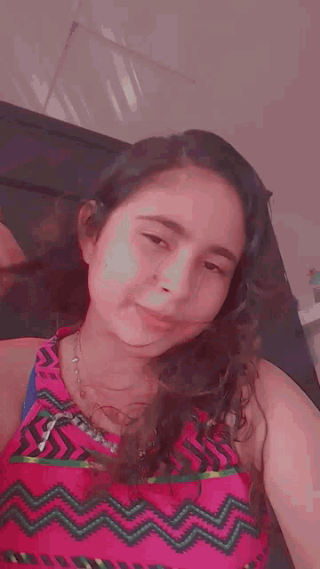 a young woman is taking a selfie in front of a mirror while wearing a pink top and a blue tank top .