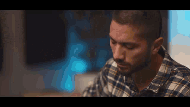 a man wearing a plaid shirt is looking down at something
