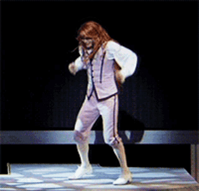 a woman with long red hair is dancing on a stage in a white suit