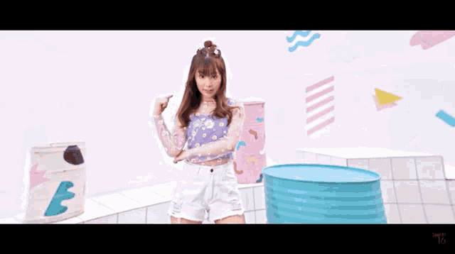 a girl in a purple top and white shorts is standing next to a blue barrel with the number 16 written on it