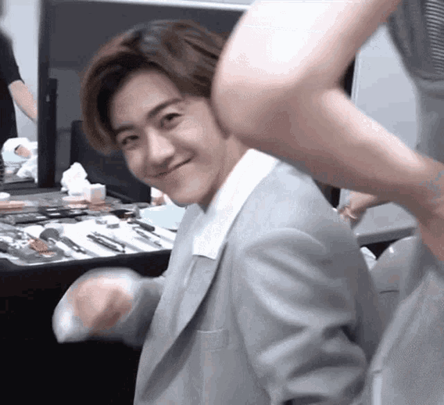 a man in a suit is standing in front of a table with makeup on it and smiling .