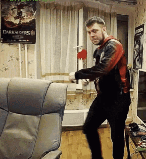 a man is dancing in a living room with a poster for darksiders on the wall