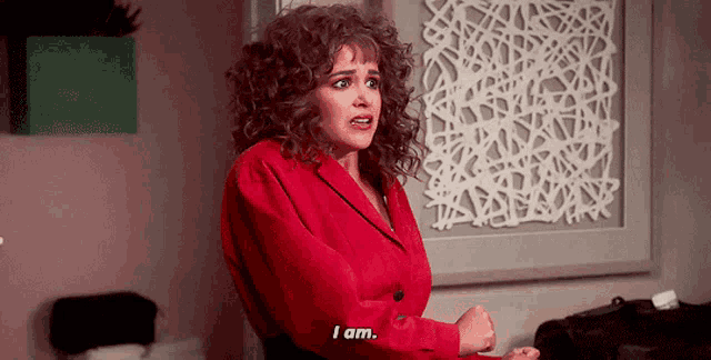 a woman in a red jacket is standing in front of a wall and says i am .