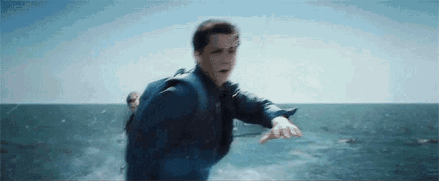 a man in a life jacket is pointing at something in the ocean .