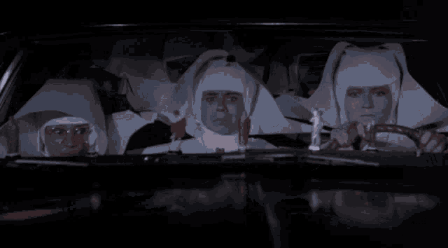 a group of nuns are sitting in a car with a statue of jesus on the windshield