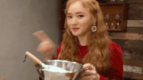 a woman in a red sweater is holding a bowl with a wooden spoon in it .
