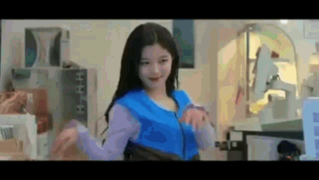 a woman in a blue jacket is dancing in front of a computer screen .