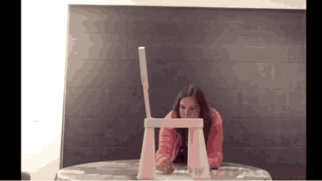 a woman is sitting at a table with a pink chair and a white object .