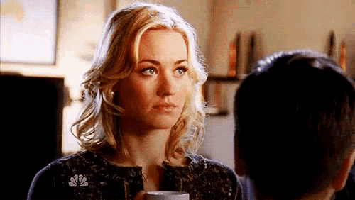 a woman is holding a cup of coffee and looking at a man in a room .