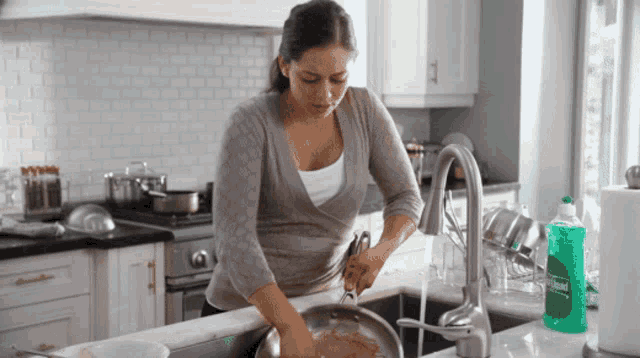 a woman is washing dishes in a kitchen with a bottle of dish soap in the sink