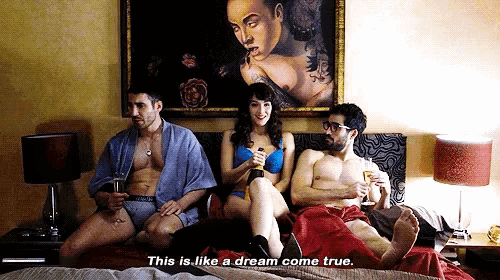 two men and a woman are sitting on a bed and one of them says this is like a dream come true