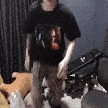 a man in a black t-shirt is standing in a room with a chair .
