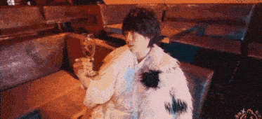 a woman in a fur coat is sitting on a couch holding a wine glass .