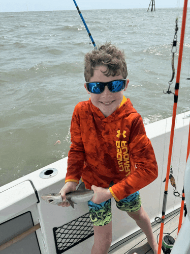 a young boy wearing an under armour shirt is holding a small fish