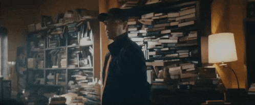 a man is standing in front of a bookshelf filled with books and a lamp
