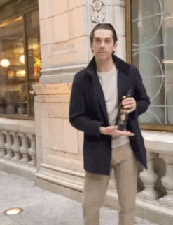 a man in a black jacket is standing in front of a building holding a bottle