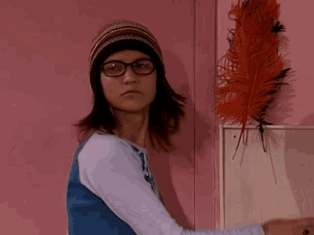 a young girl wearing glasses and a hat is standing in front of a pink wall .