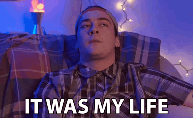a man in a plaid shirt is laying on a bed with the words it was my life above him