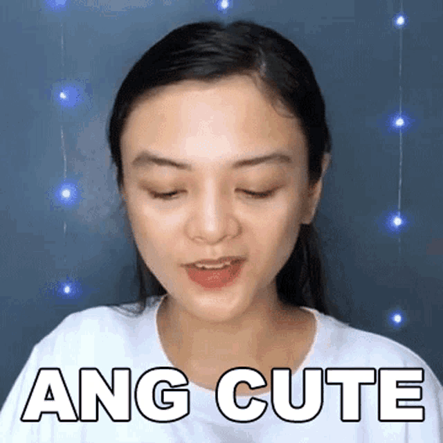 a woman is wearing a white shirt and making a funny face with the words ang cute written on it .