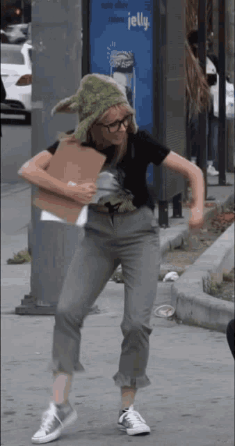 a woman in a green hat is holding a cardboard box in front of a sign that says jelly