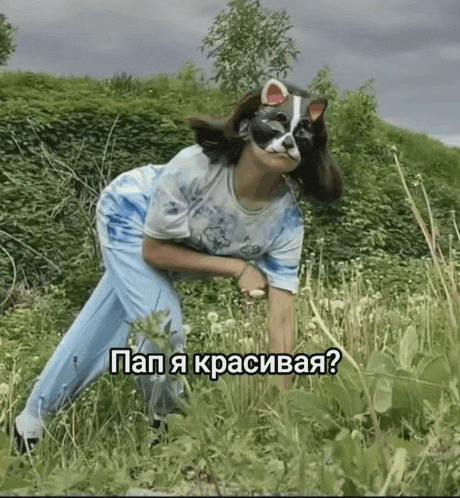 a woman wearing a cat mask is kneeling in a field with a caption in russian