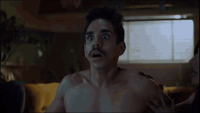 a shirtless man with a mustache looks surprised