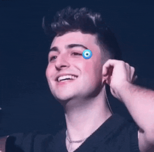 a young man is smiling and touching his ear while wearing ear buds .