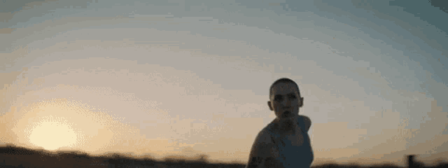 a man with a tattoo on his arm is running on a beach at sunset .