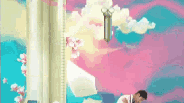 a man is sitting in front of a colorful wall with flowers and clouds .