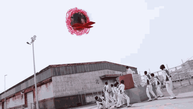 a group of people are standing in front of a building with a red object flying in the sky