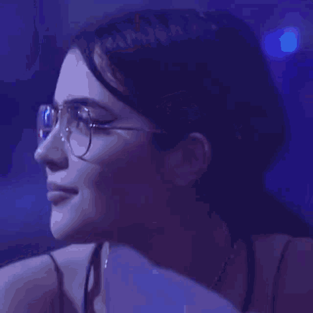a woman wearing glasses and a necklace is blowing soap bubbles