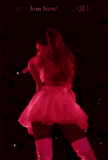 a woman in a pink dress and boots is singing into a microphone on a stage .