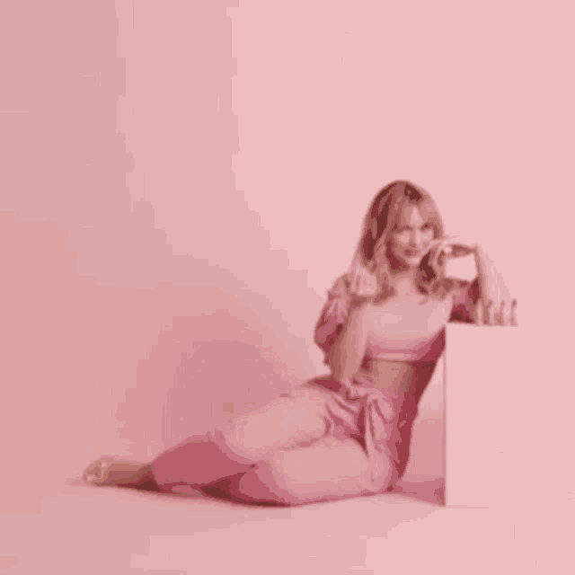 a woman in a pink outfit is sitting on the floor with her legs crossed .