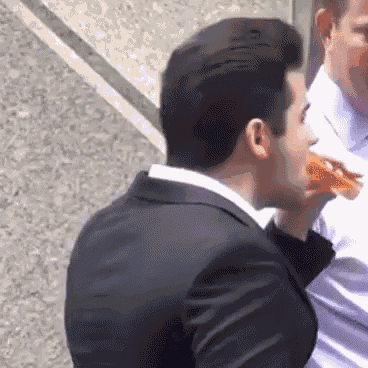 a man in a suit is eating a slice of pizza .