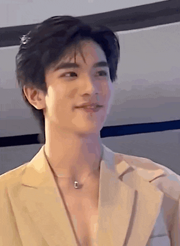 a young man wearing a tan jacket and a necklace is smiling .