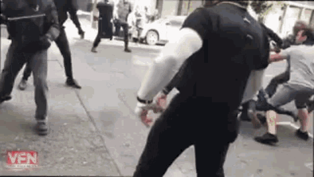 a group of people are standing on a sidewalk fighting each other .