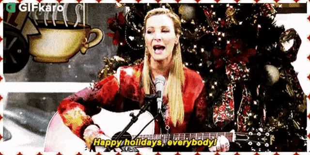 a woman is singing into a microphone while holding a guitar and a christmas tree in the background .