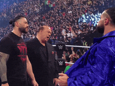 a man in a blue jacket is standing in front of a wrestling ring