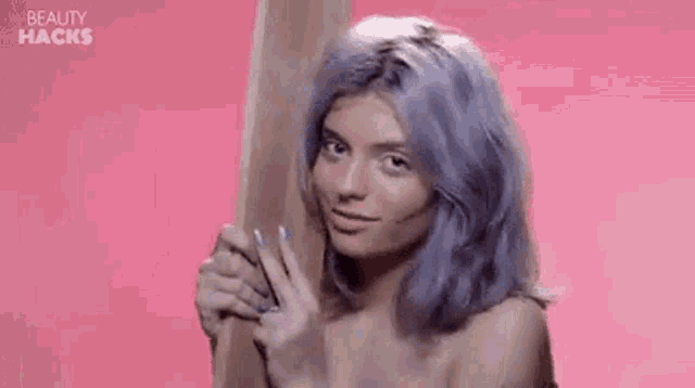 a woman with purple hair is smiling while holding a wooden stick .